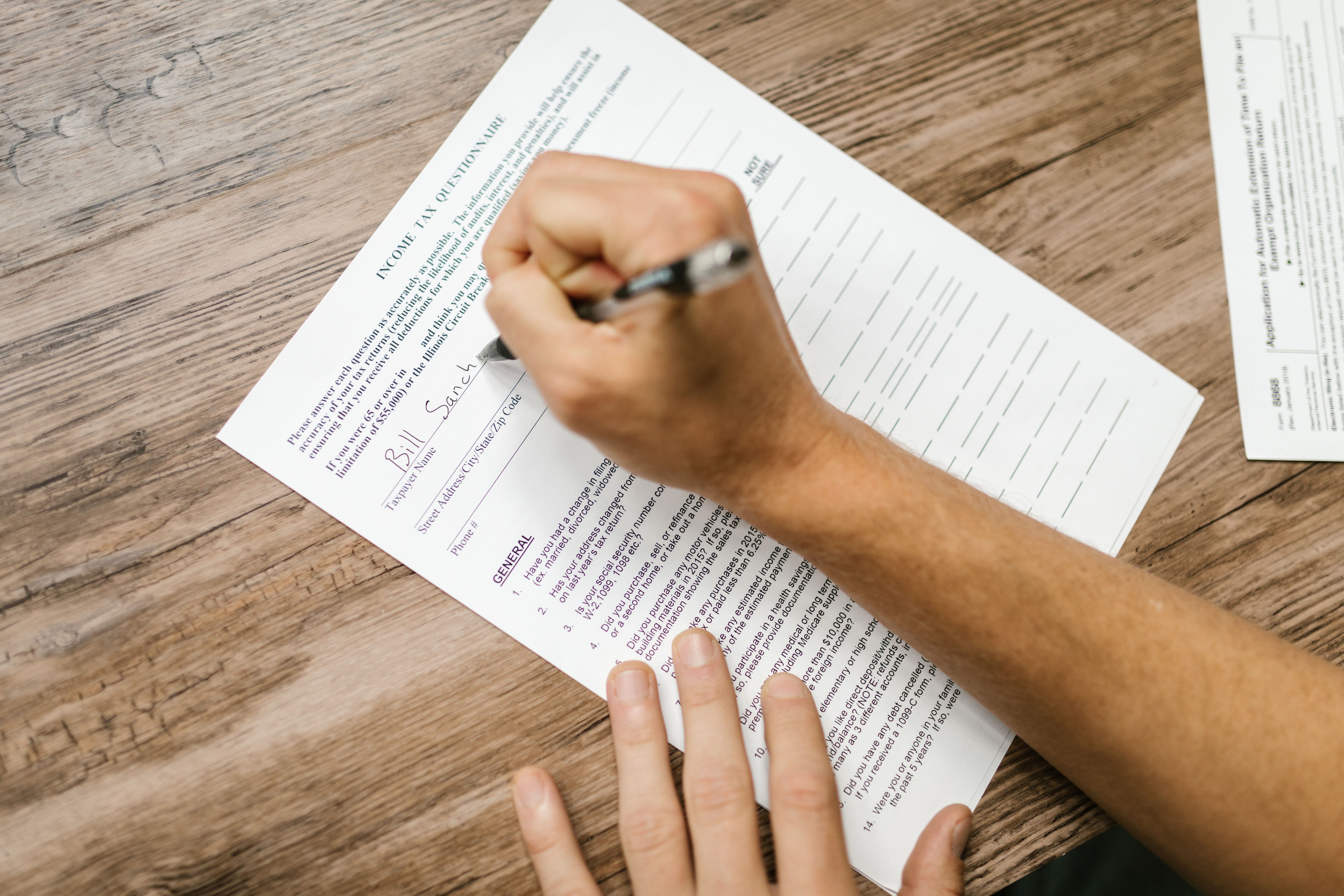 A person filling ouy=t a tax form on a desk with a pen
